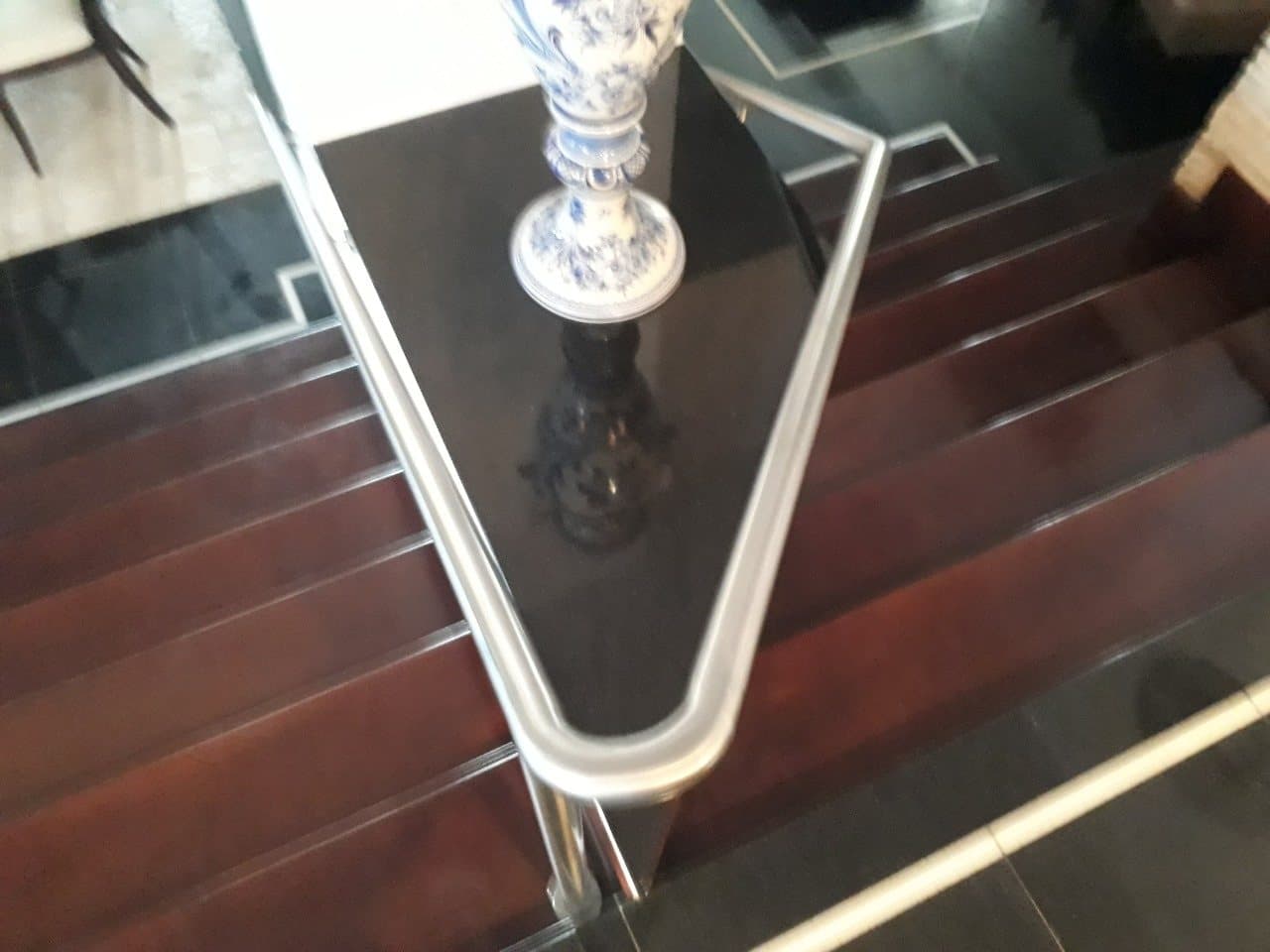 Curva do corrimão em aço inox vista de cima, sobre o patamar em granito preto