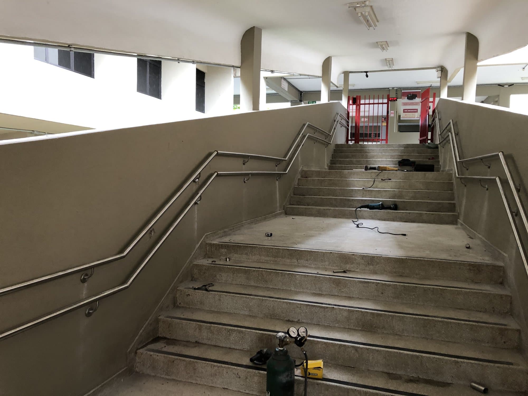 Escadaria larga com corrimãos duplos em aço inox fixados nas paredes laterais