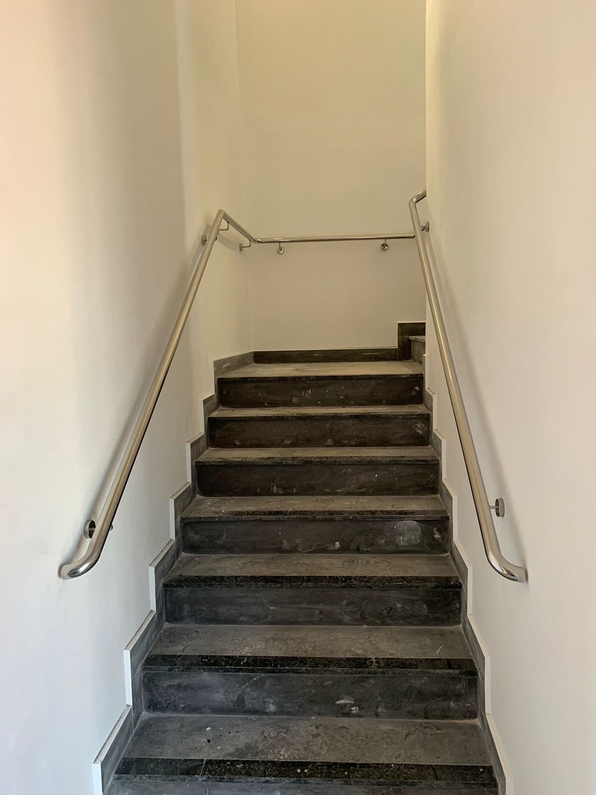 Escada de granito escuro com corrimãos em aço inox fixados nas duas paredes