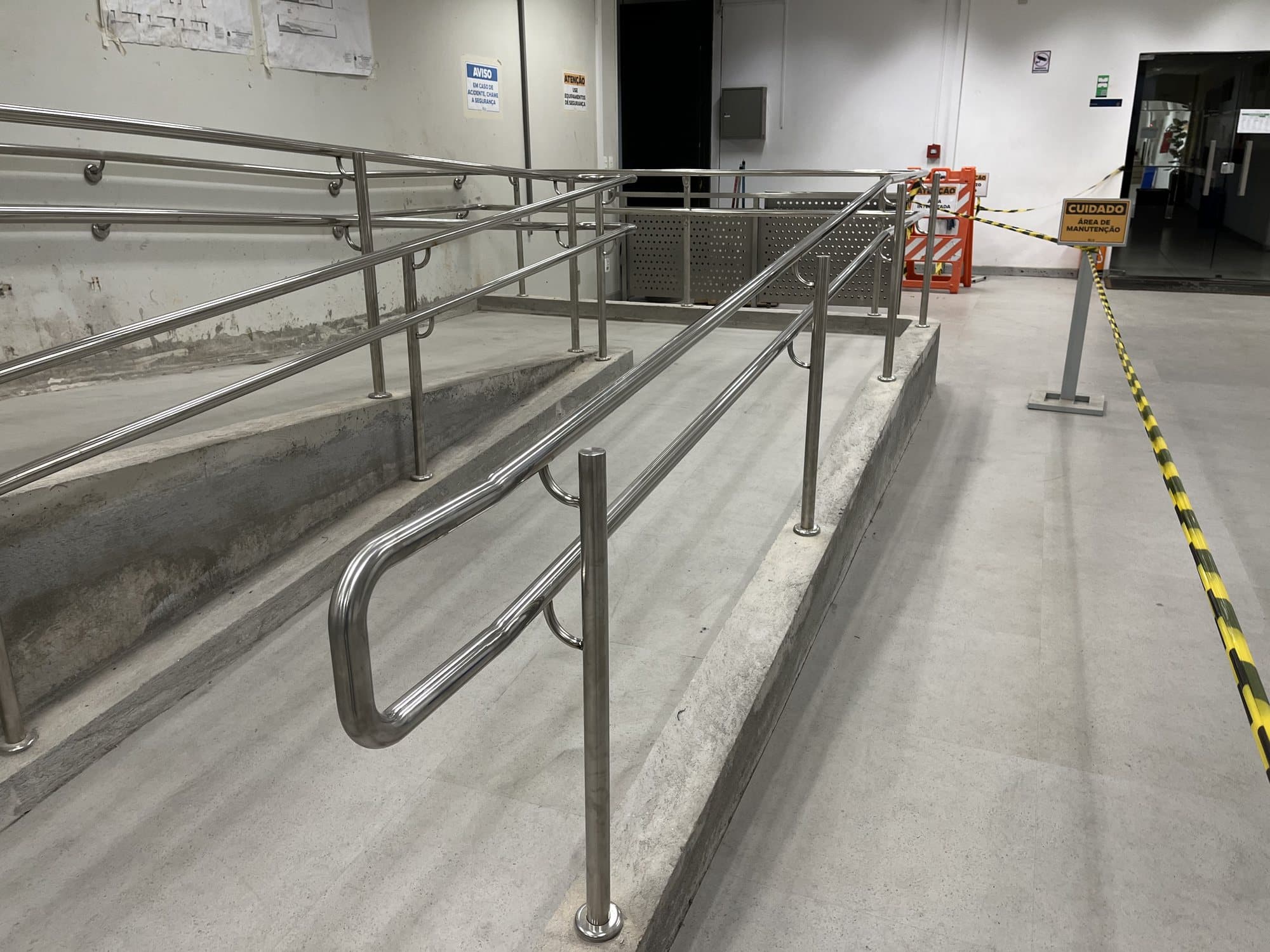 Trecho de rampa com corrimãos duplos em aço inox fixados na parede e em montantes
