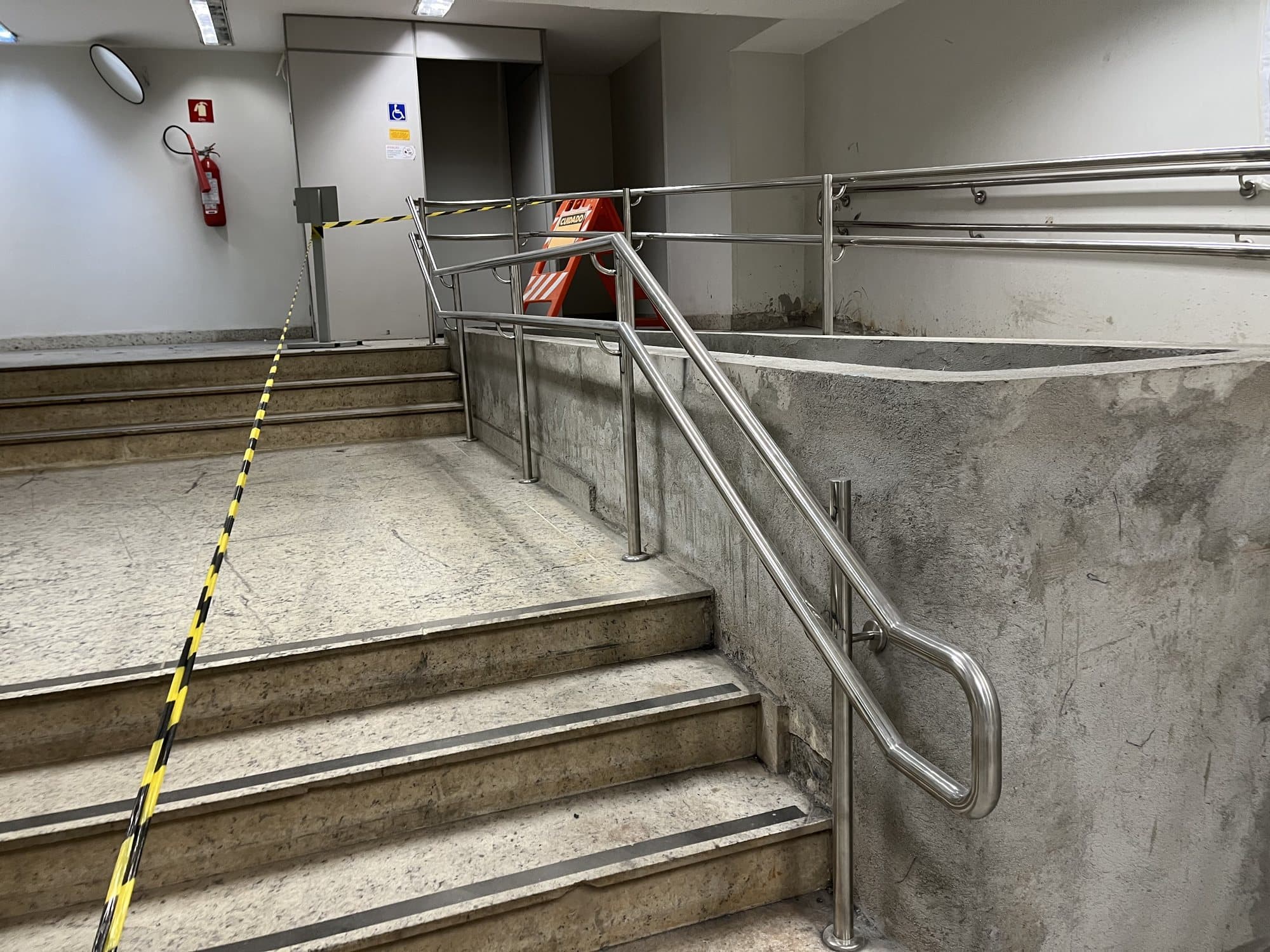 Corrimão em aço inox na escada ao lado da rampa de acessibilidade