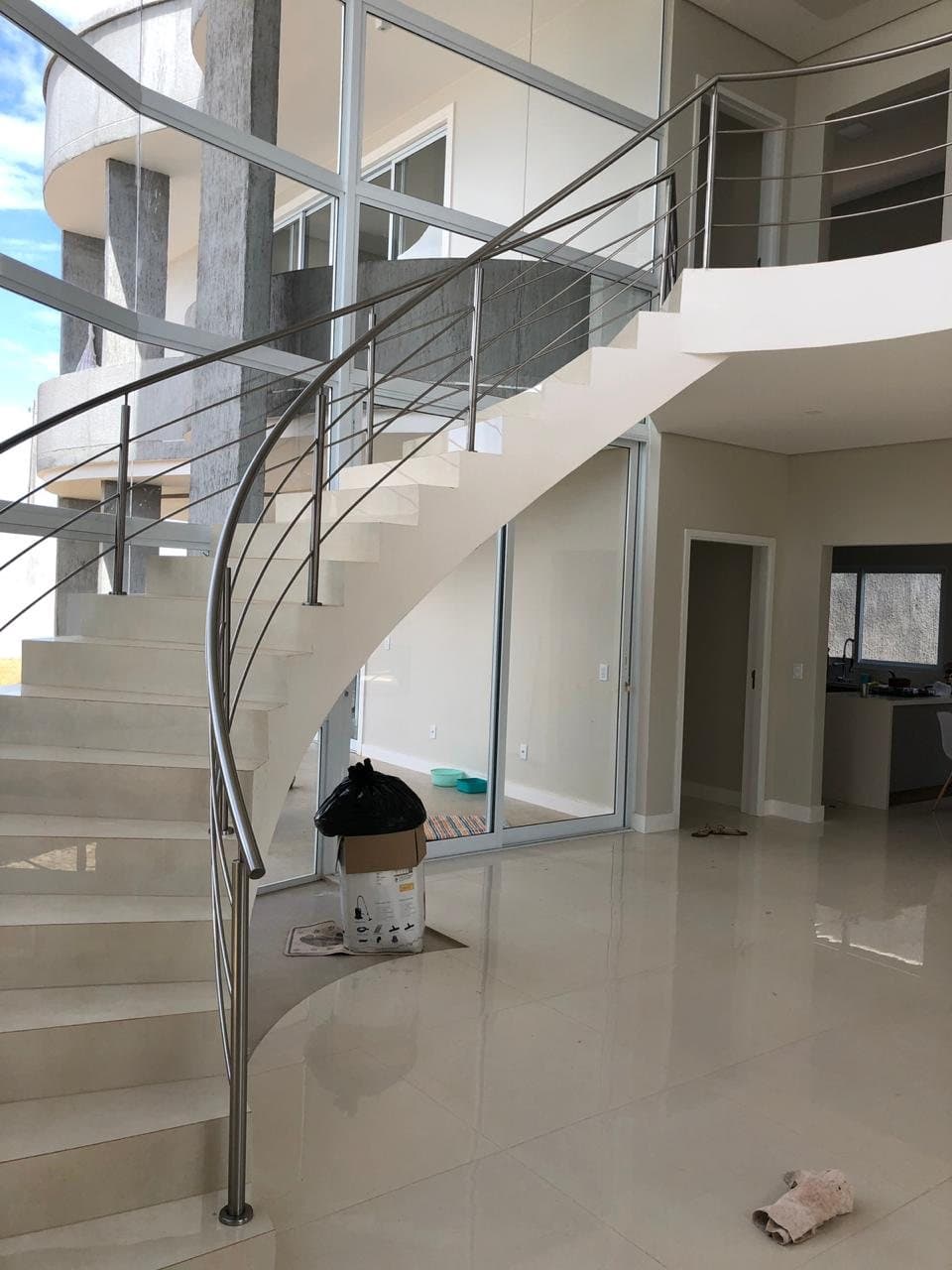 Vista geral da escada curva com corrimão e guarda-corpo em aço inox em sala de pé-direito duplo