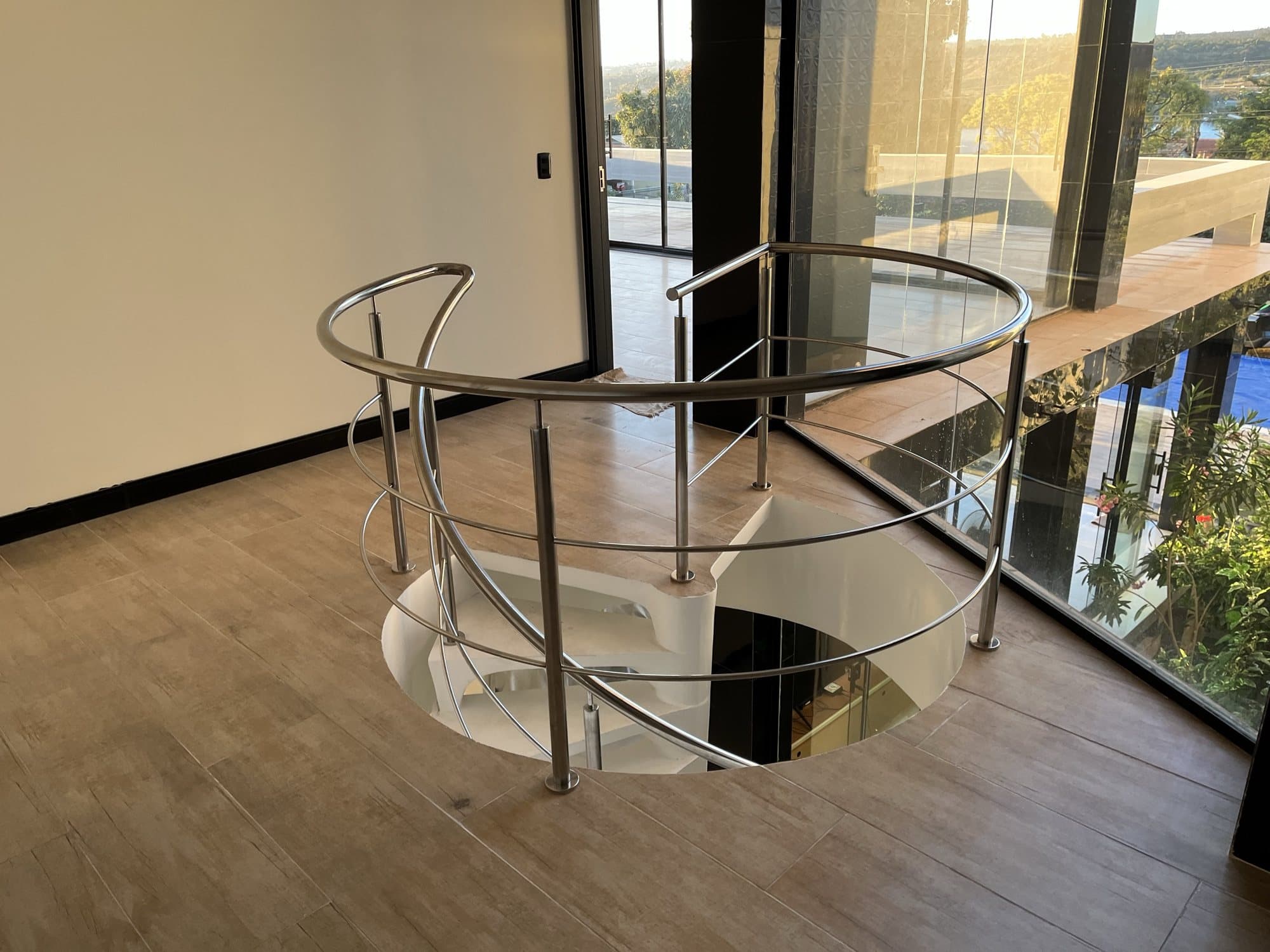 Guarda-corpo circular em aço inox ao redor da abertura de uma escada helicoidal branca, visto do pavimento superior