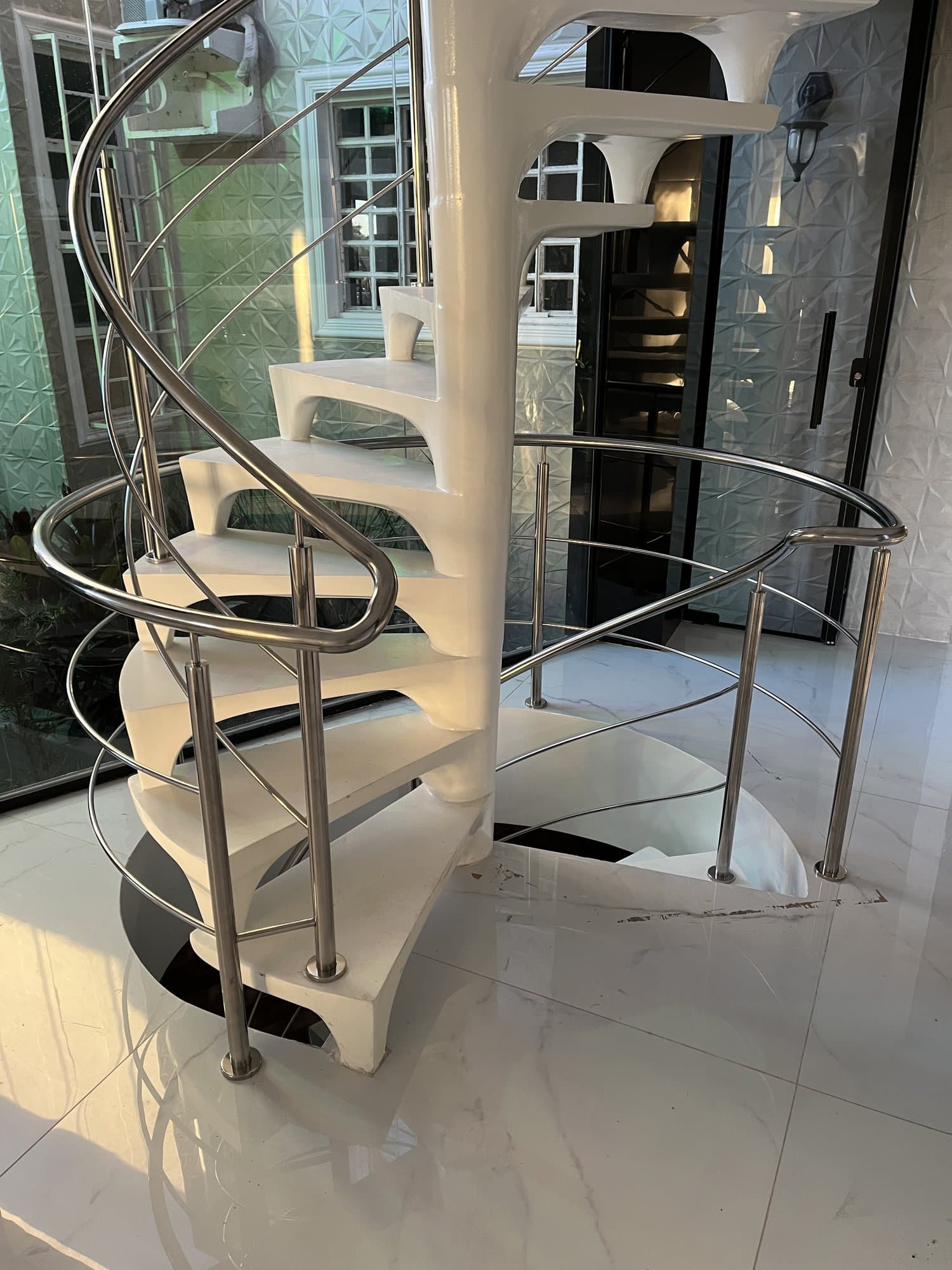 Escada helicoidal branca vista de baixo, com corrimão e guarda-corpo em aço inox acompanhando toda a subida