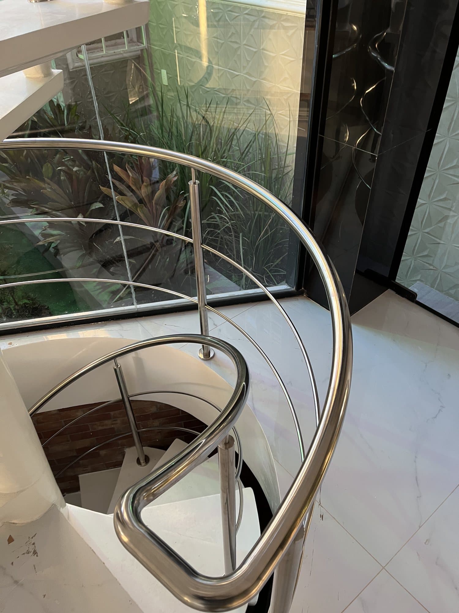 Arremate curvo do corrimão em aço inox no topo da escada helicoidal, visto de cima