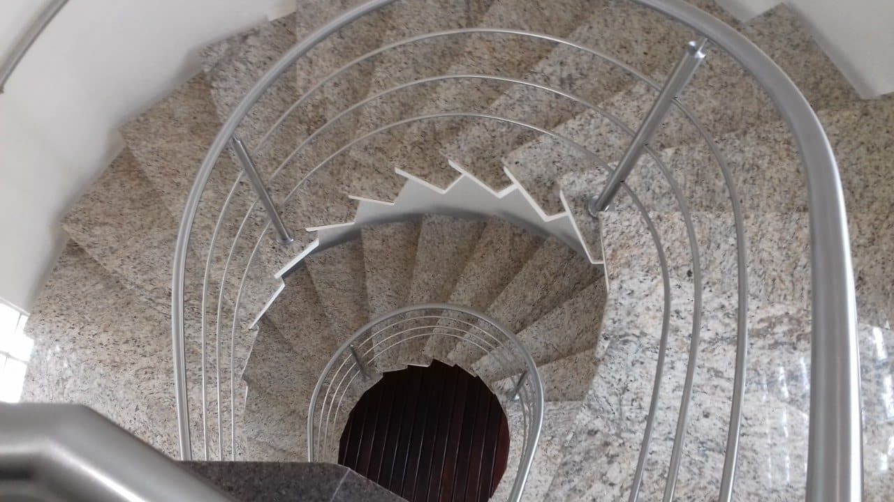 Escada helicoidal em granito vista de cima, com guarda-corpo em aço inox de tubos curvados