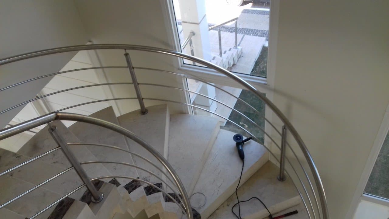 Escada helicoidal em mármore claro com guarda-corpo em aço inox, vista do pavimento superior