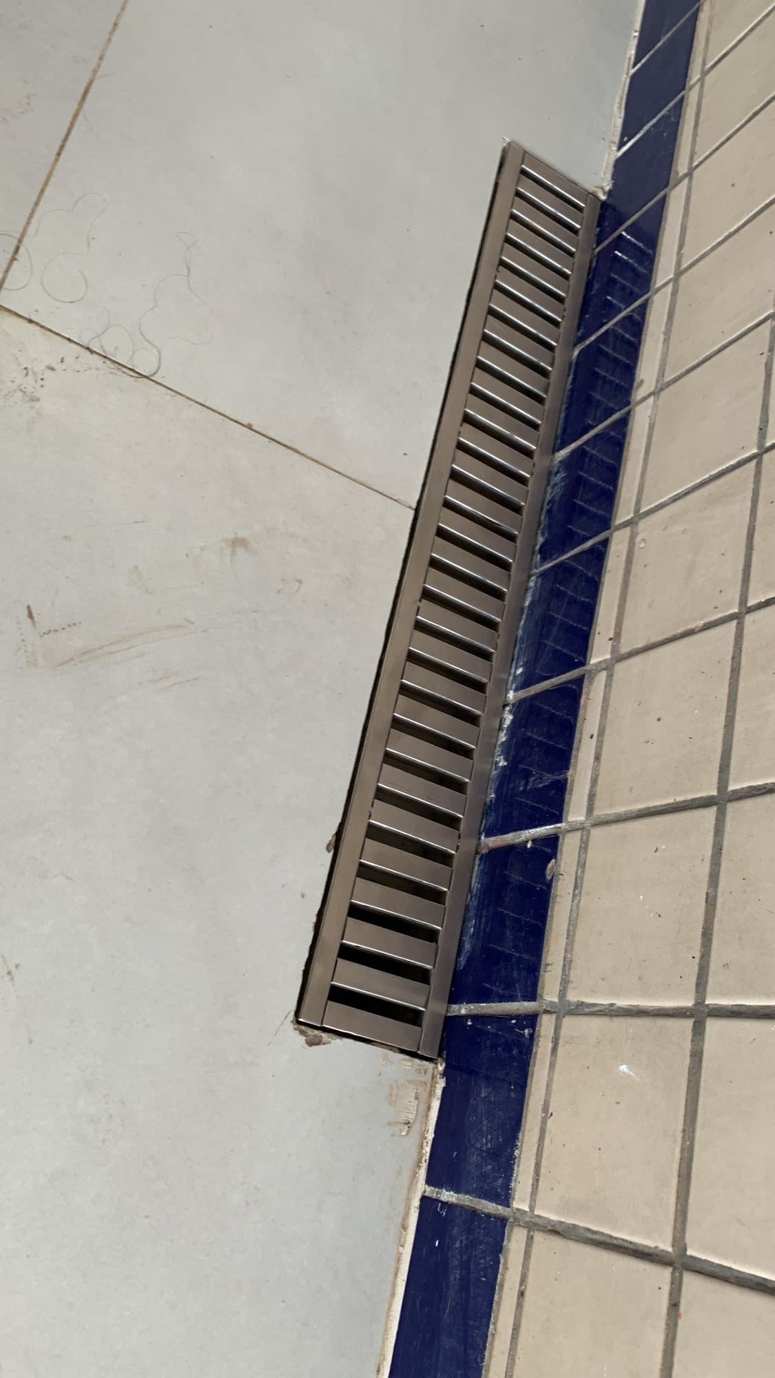 Grelha linear em aço inox instalada no piso, junto a uma parede de azulejos