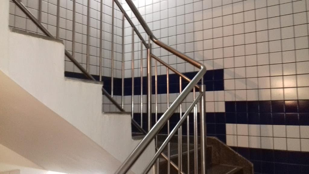 Guarda-corpo em aço inox com balaústres verticais na virada de uma escada com parede de azulejos