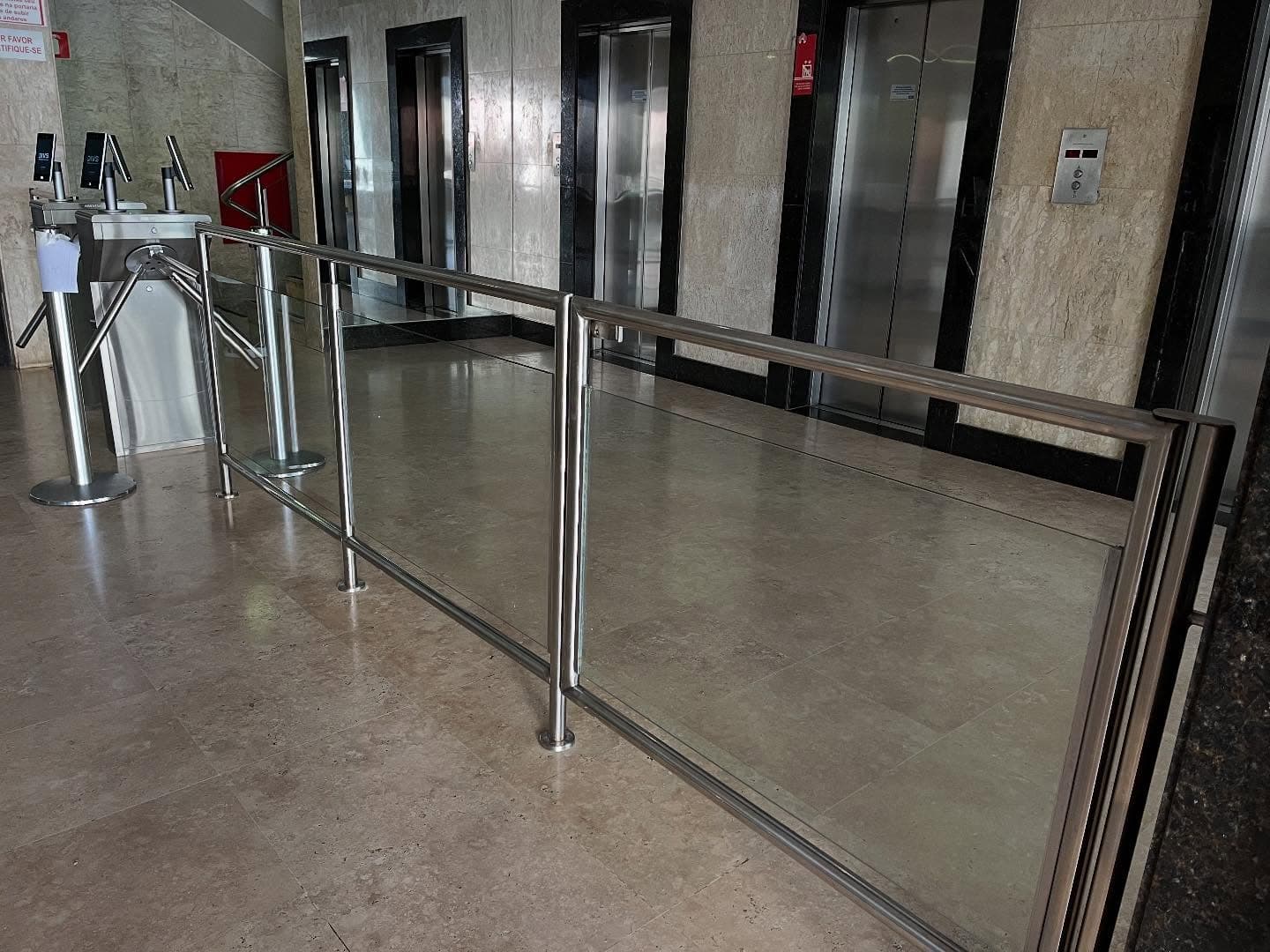 Guarda-corpo em aço inox com painéis de vidro em hall de edifício, ao lado das catracas de acesso