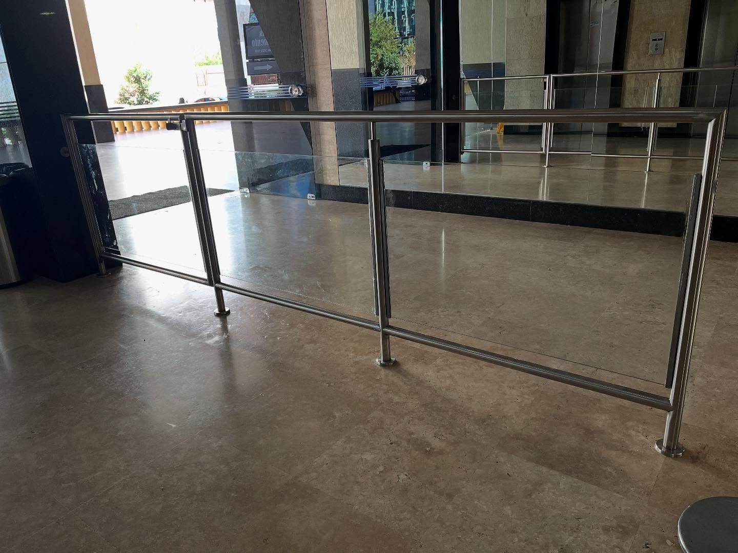 Trecho do guarda-corpo em aço inox e vidro fixado ao piso de mármore do hall