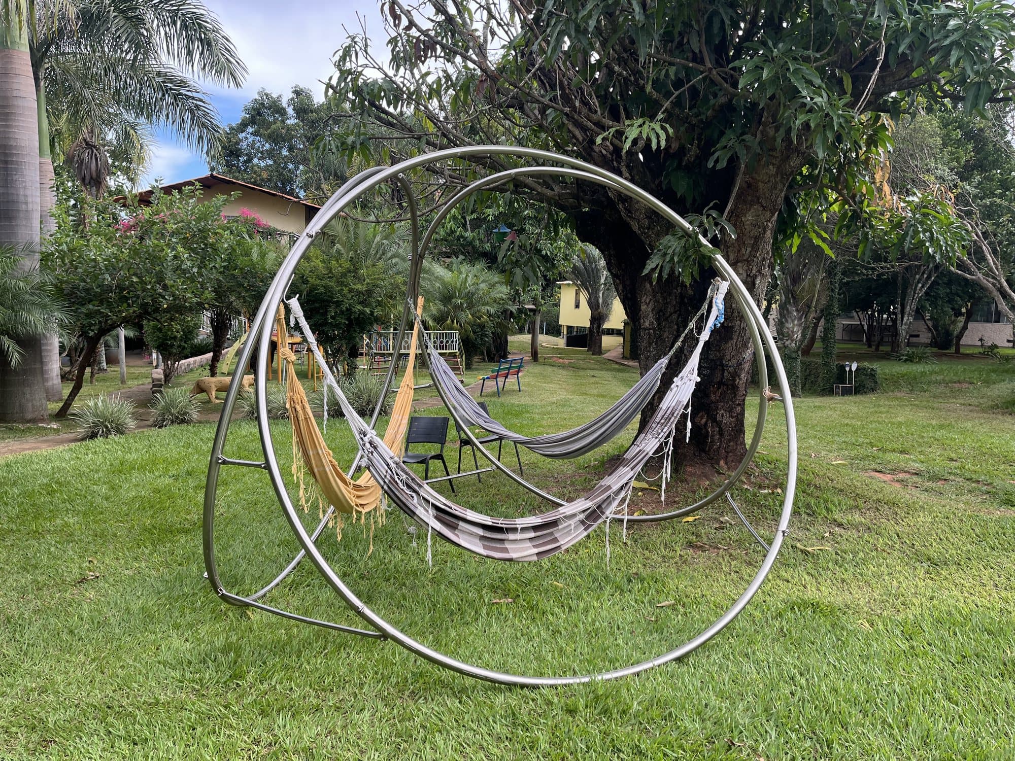 Estrutura circular em aço inox com duas redes de descanso penduradas, instalada em um gramado